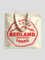 Tote bag naturale Redland Tours con grafica rossa effetto timbro da viaggio.