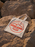 Tote bag naturale Redland Tours con grafica rossa effetto timbro da viaggio.