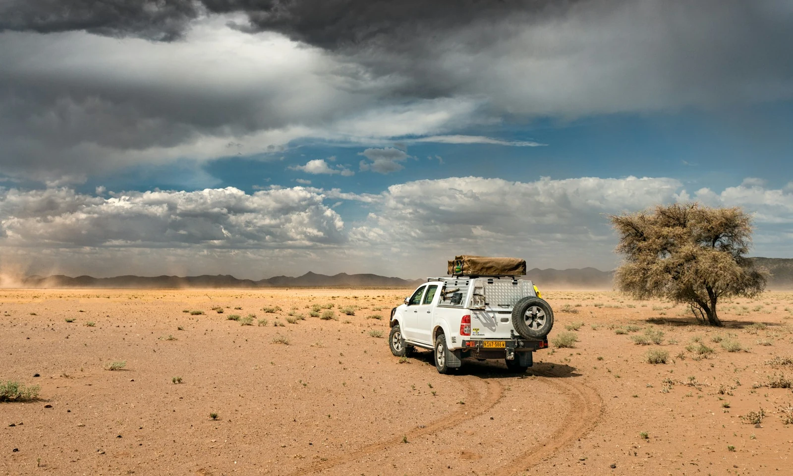 An equipped 4×4 travels across the Namibian desert under a sky of clouds