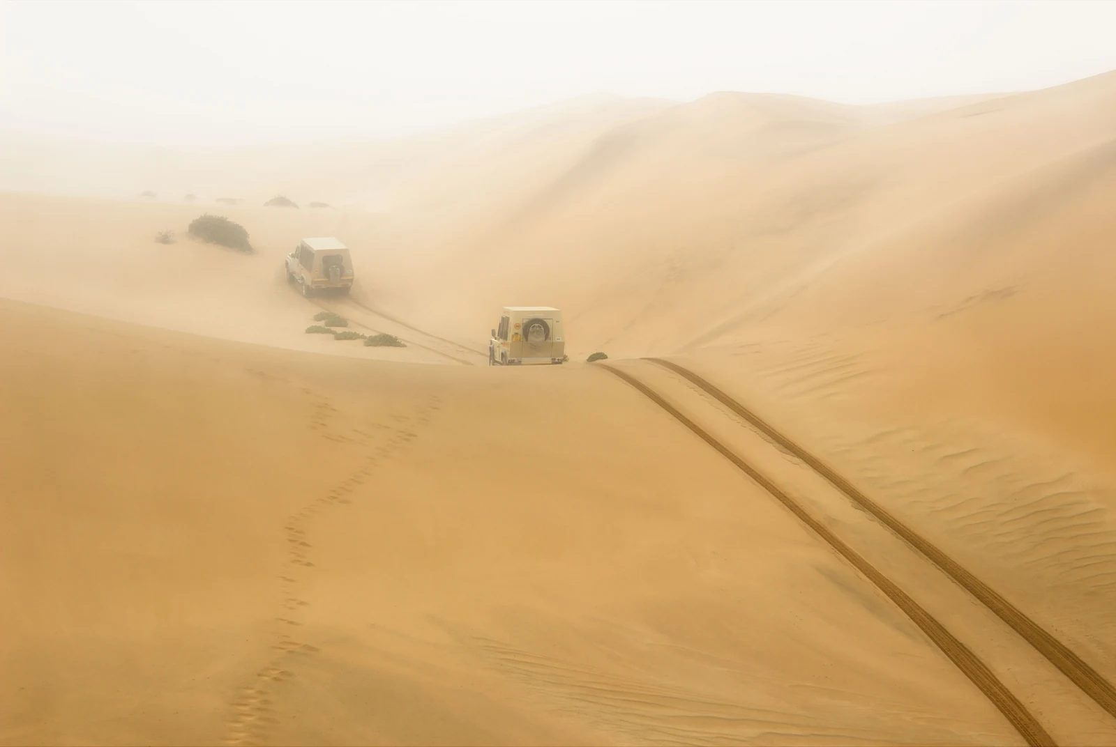 Zwei Fahrzeuge überqueren die Dünen Namibias zwischen Sand und goldenem Licht